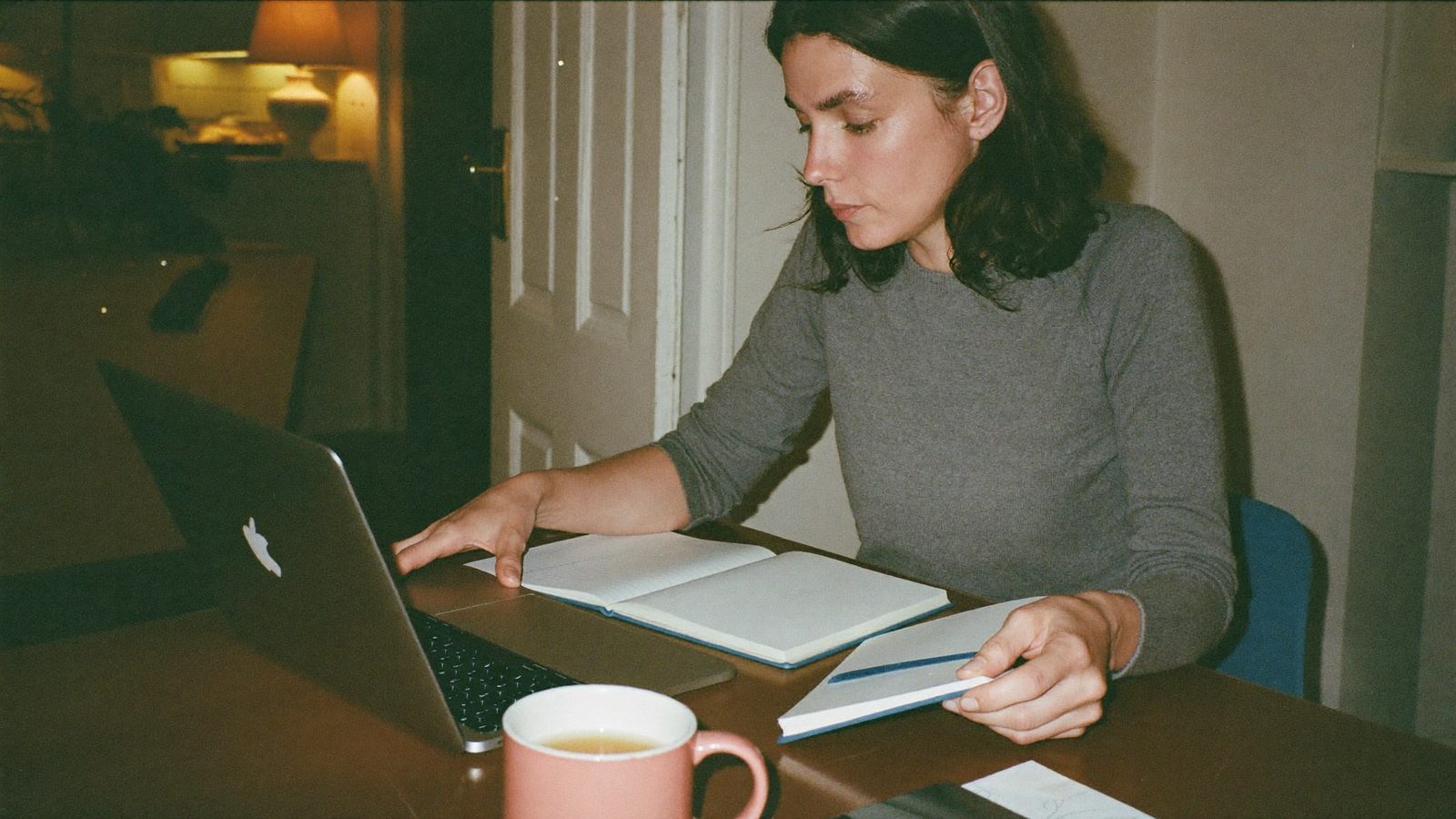 Una donna adulta studia la sera al tavolo di casa con il laptop e un quaderno.