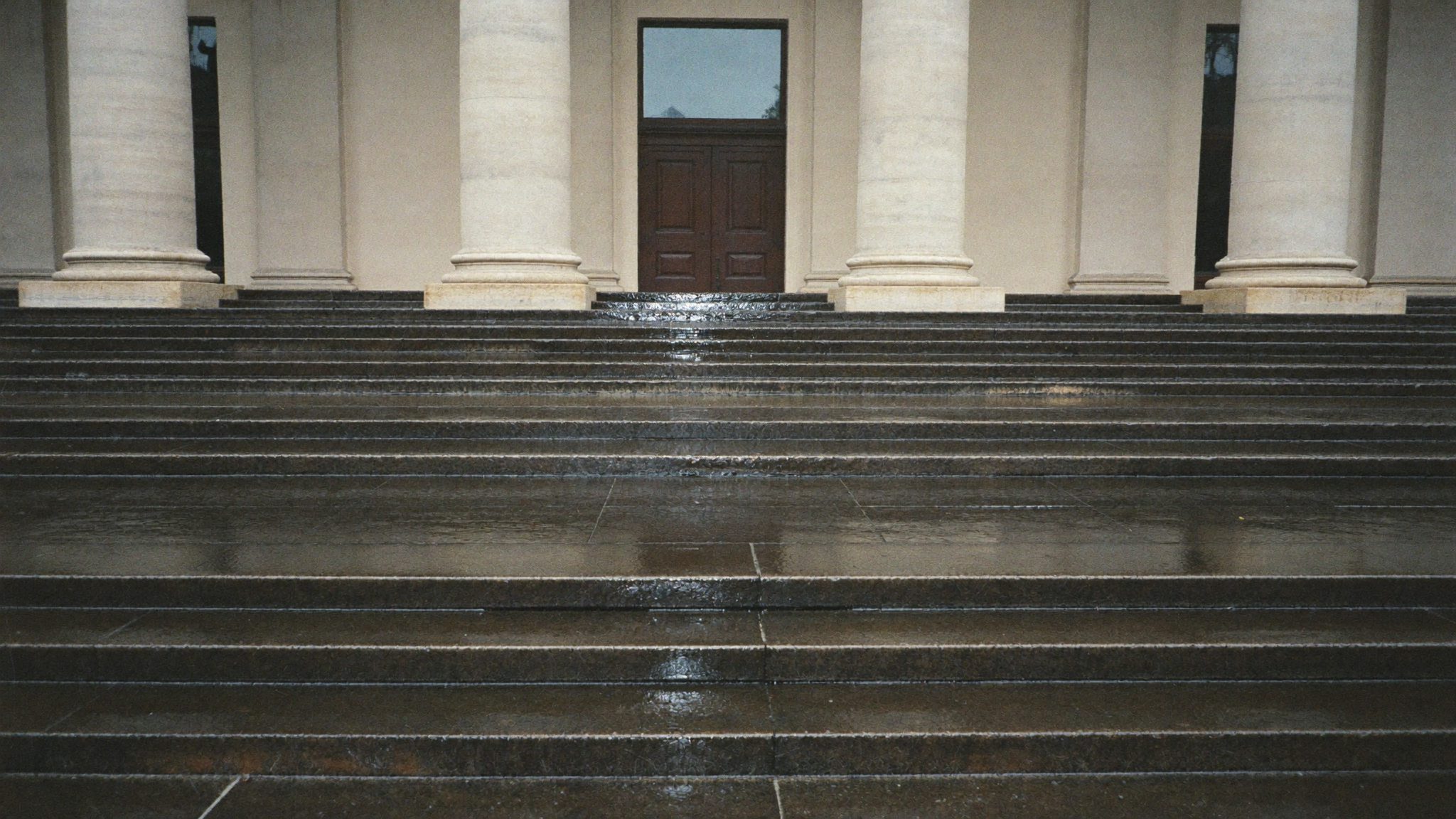 Scalone in pietra di un palazzo pubblico bagnato dalla pioggia, con le colonne e un portone di legno chiuso in cima