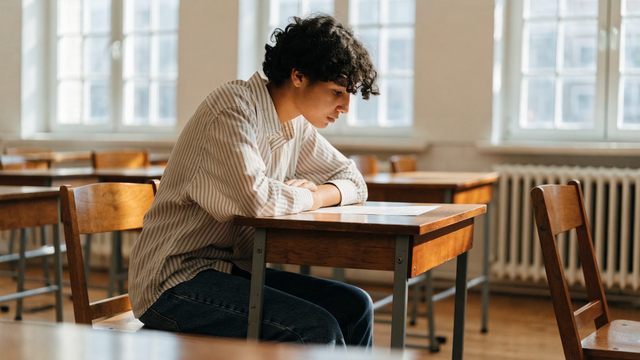 Studente seduto a un banco scolastico con libri e appunti, atmosfera seria e concentrata